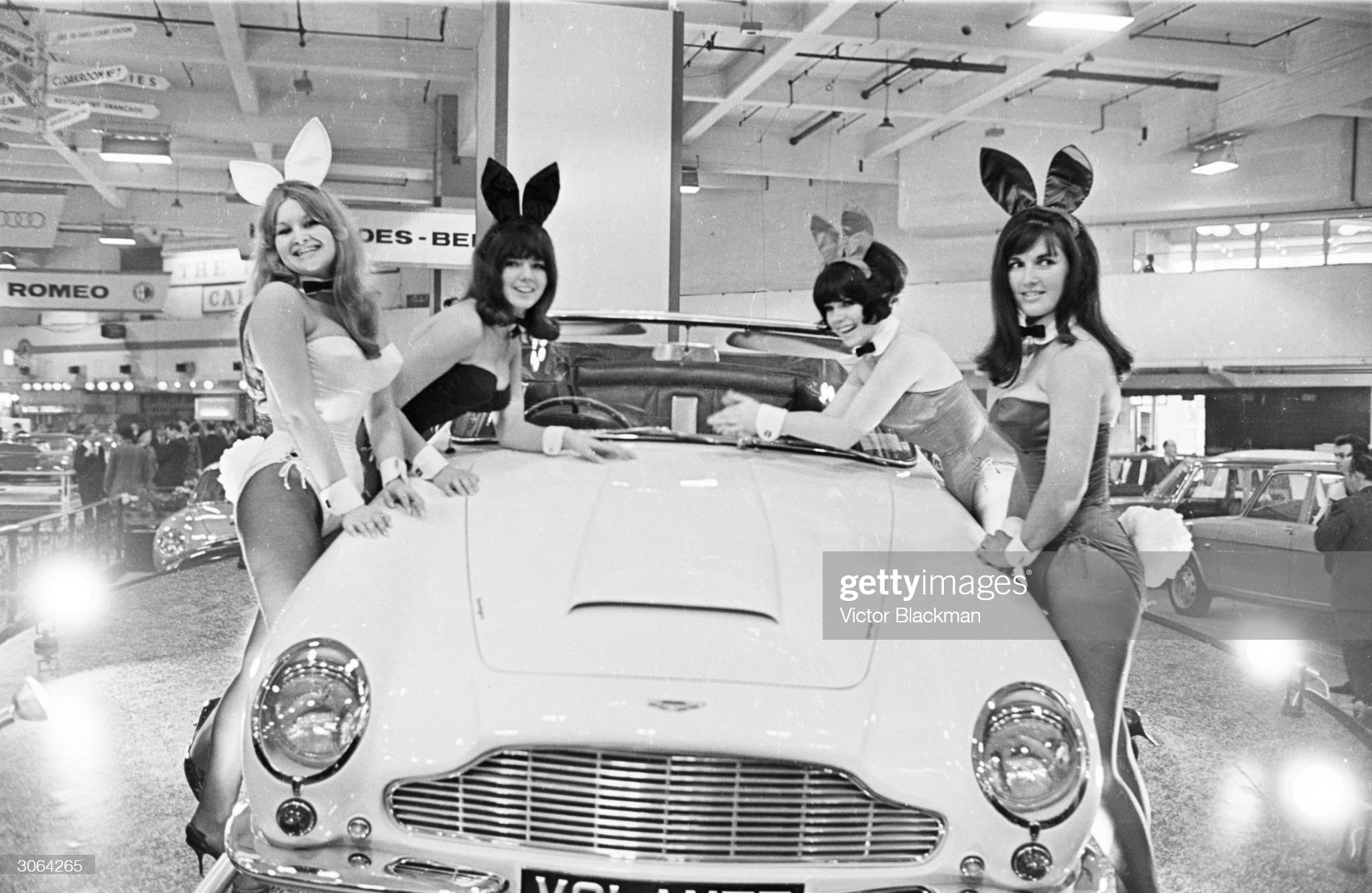 19th October 1965: a group of bunny girls sitting on an Aston Martin Volante at a motor show at Earl's Court. 
