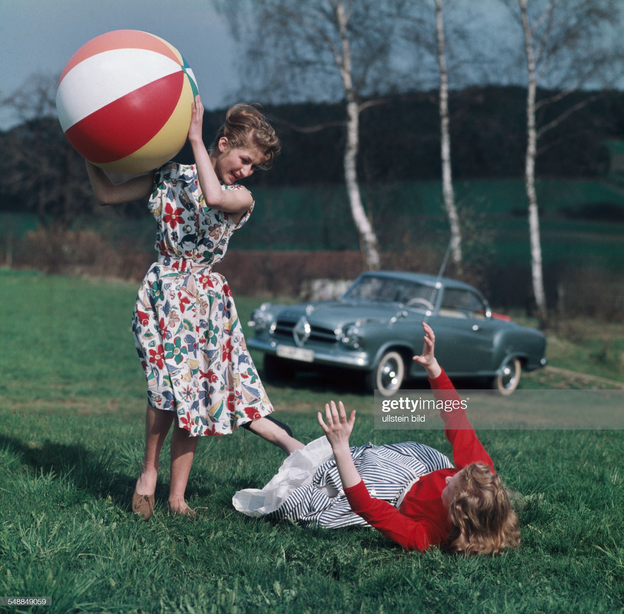Germany Bavaria: two young women are playing with a beach ball on a meadow in 1955, in the background a Borgward Isabella coupe. 