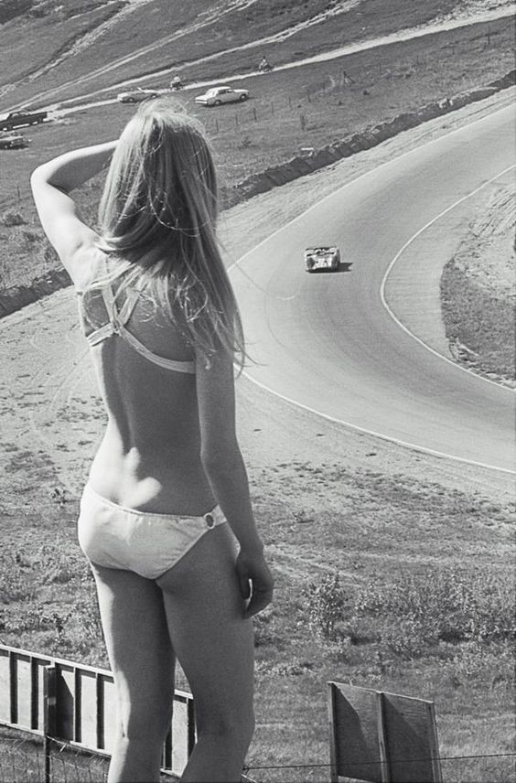 A girl in a bikini watching a car race.