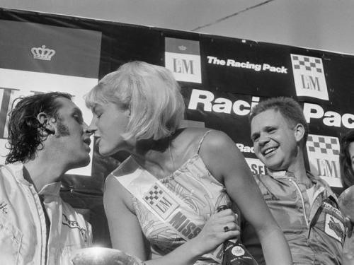 A vintage grid girl kissing a driver on the podium.