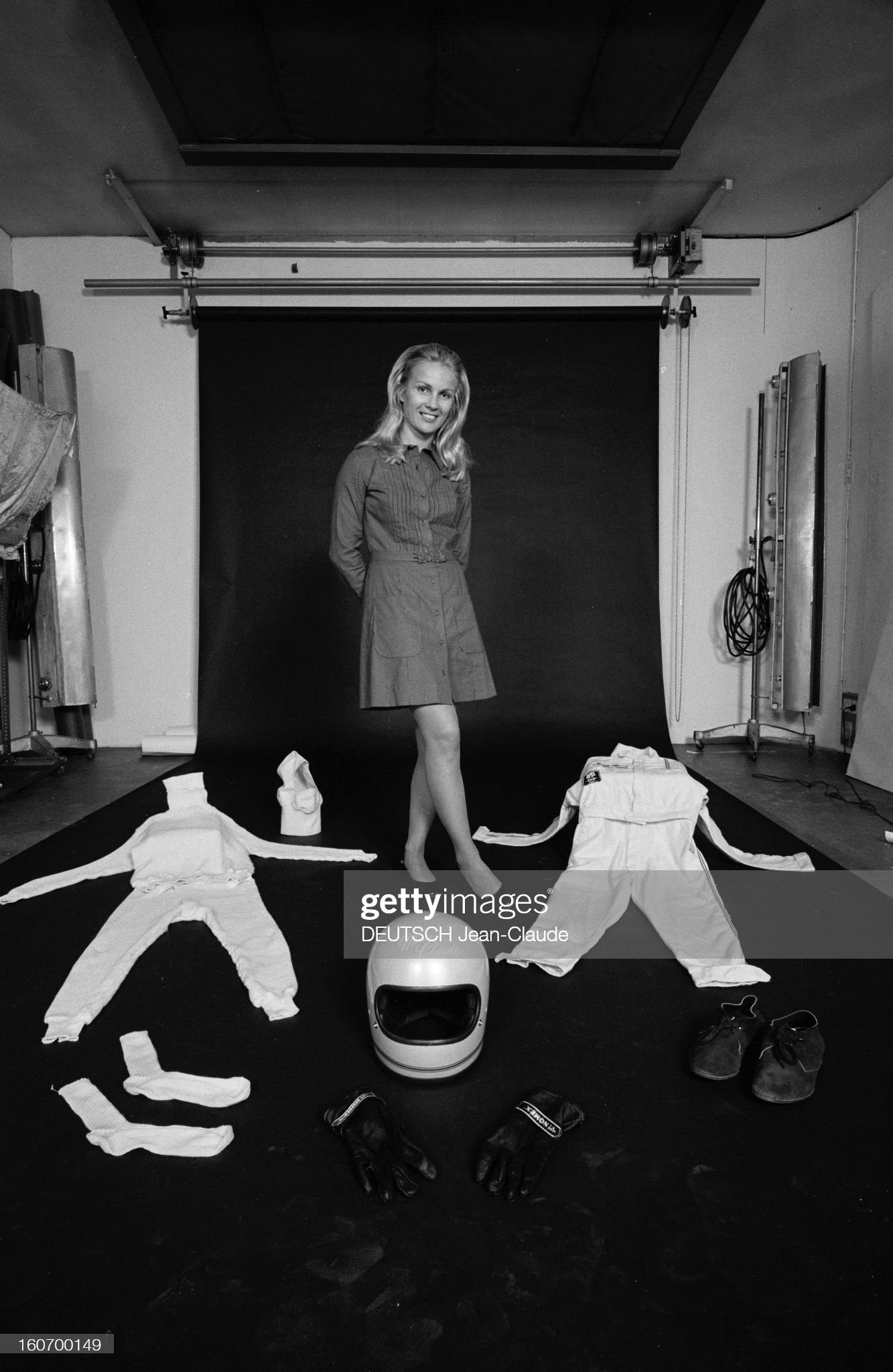 Marie-Claude Beaumont, race car driver, in France in June 1971 on the occasion of her first participation in the 24 Hours of Le Mans, wearing a short dress, posing with her equipment on the ground, overalls, helmet, shoes and gloves. 