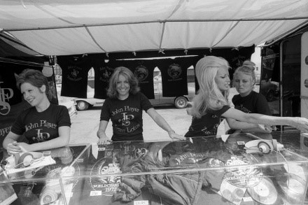 The JPS girls try their hands at selling merchandise from the official Lotus stand. British Grand Prix, Rd 9, Silverstone, England, 14 July 1973.