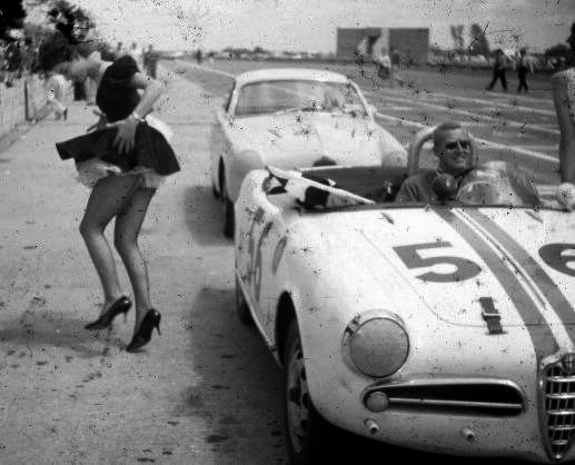 A driver in his racing car and a beautiful girl.