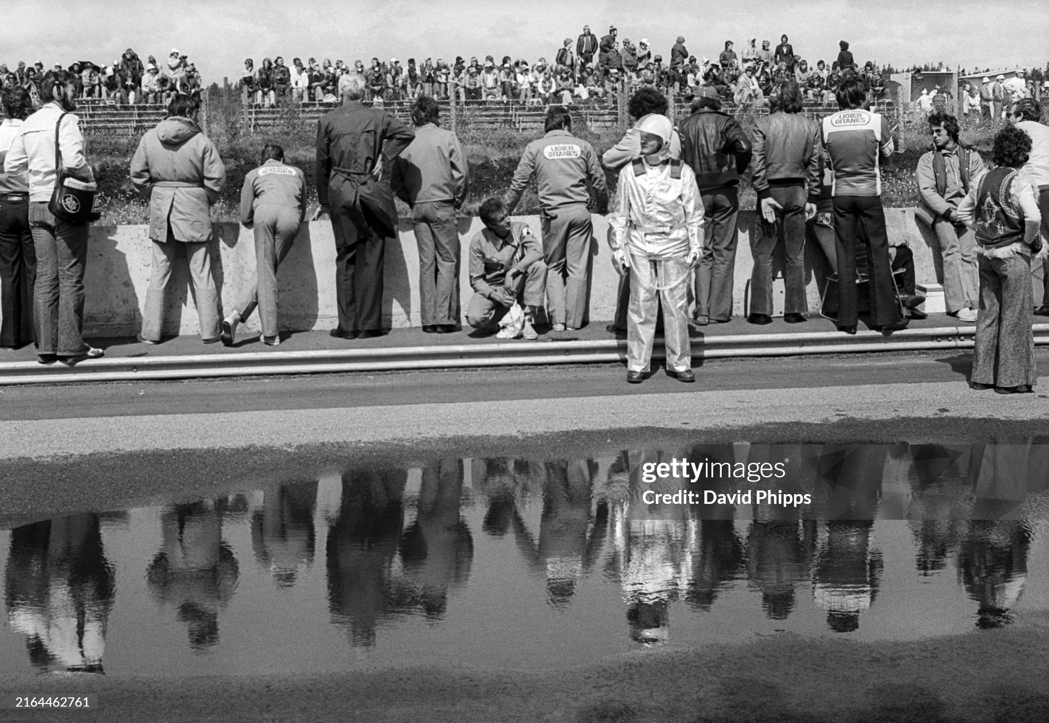Those on the pit wall are reflected in a puddle in the pit lane during the Grand Prix of Sweden in Anderstorp on 13 June 1976. 