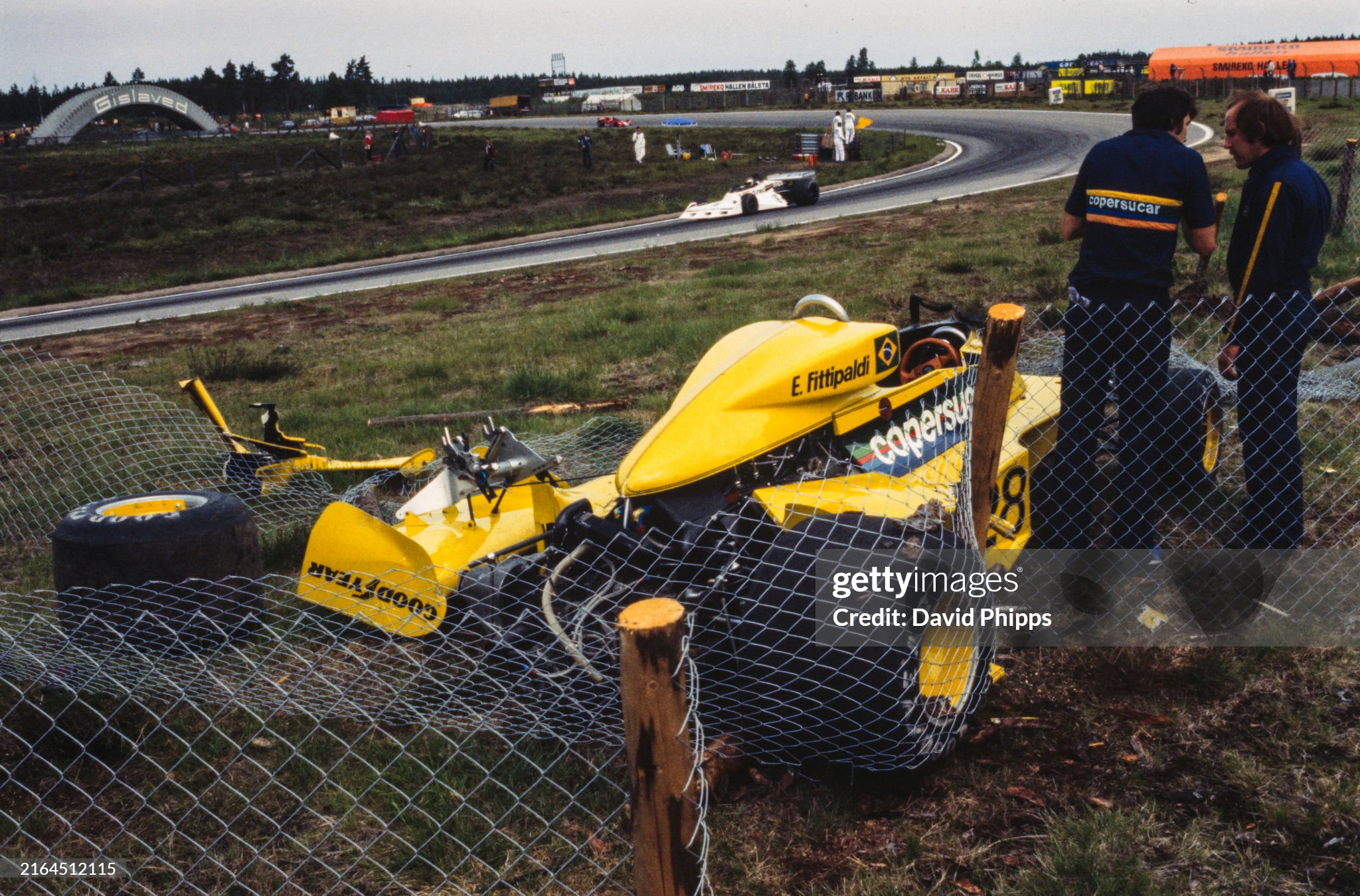The damaged Emerson Fittipaldi Fittipaldi F5 Ford, tangled in catch fencing, is guarded by team members during a practice session of the Swedish Grand Prix at Anderstorp Raceway on June 19 1977. 