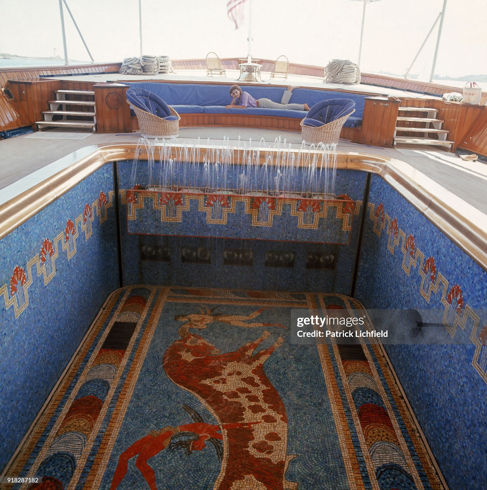 Aboard Aristotle Onassis's yacht, the ‘Christina’, Christina Onassis lays on a large couch in the sitting area above the mosaic swimming pool with waterwall and Greek designs, including a copy of the Toreador Fresco from Knossos. 