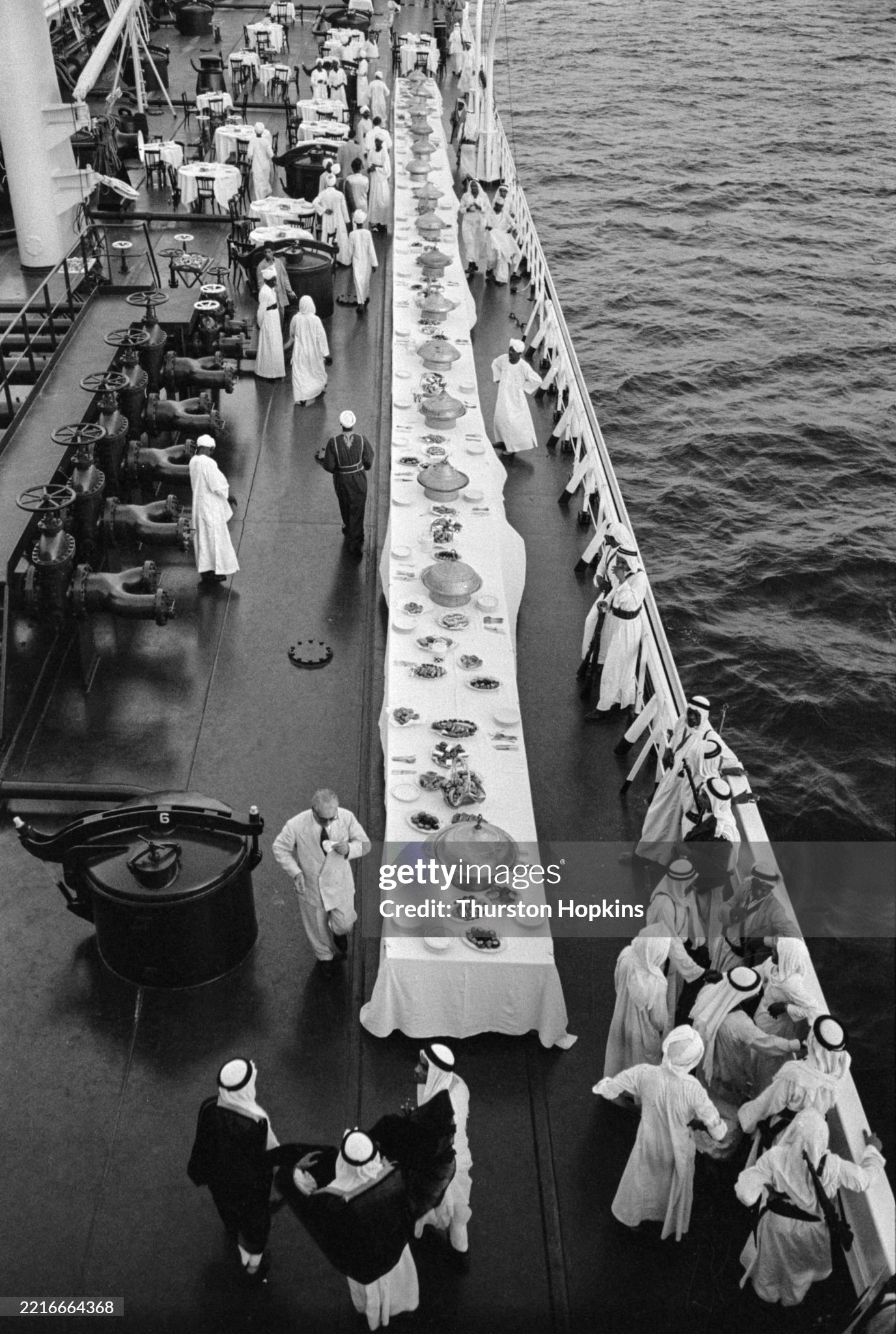 Aerial view of guests standing near an extended dining table on the deck of the Al-Malik Saud Al-Awal, an oil tanker belonging to shipping magnate Aristotle Onassis and anchored off Jeddah, Saudi Arabia, in July 1955. 