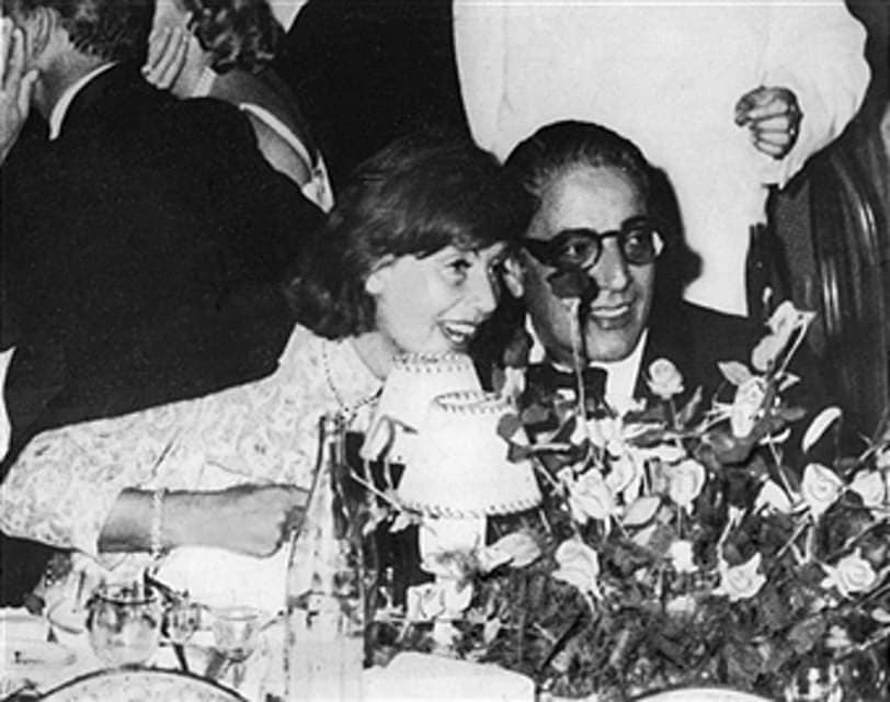 Greta Garbo, long noted as a dodge of cameras, is unaware of the photographic eye as she smiles across the table at a gala party on in Monte Carlo's Sporting Club. Her companion is Aristotle Onassis, millionaire Greek ship owner. The elegant affair drew many international society figures enjoying French Riviera vacations in 1956. 