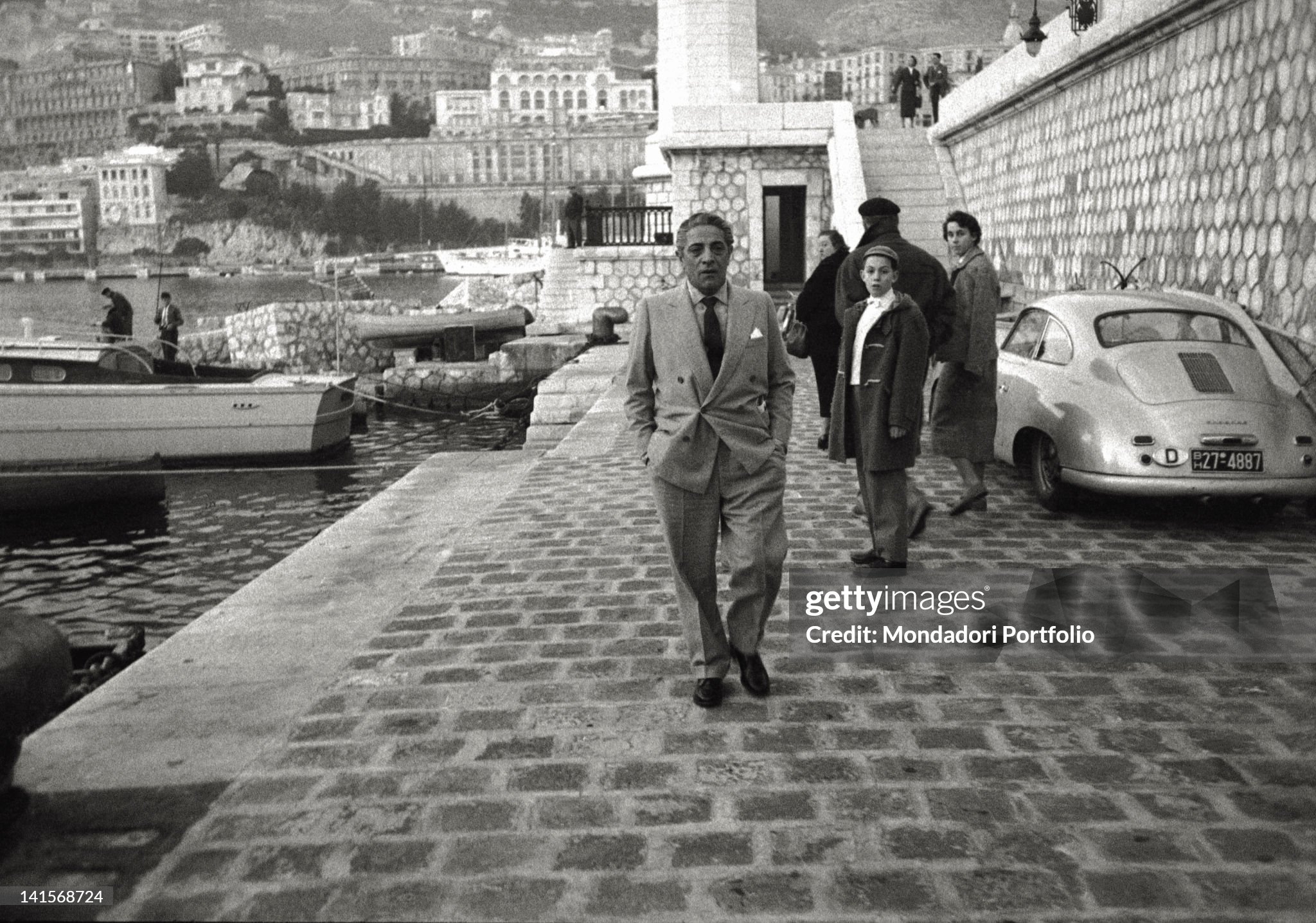 Aristotle Onassis, known by a family of tourists, photographed on the mole of Montecarlo's port, near the lighthouse, in June 1961; the Principality becomes his official residence for years. 