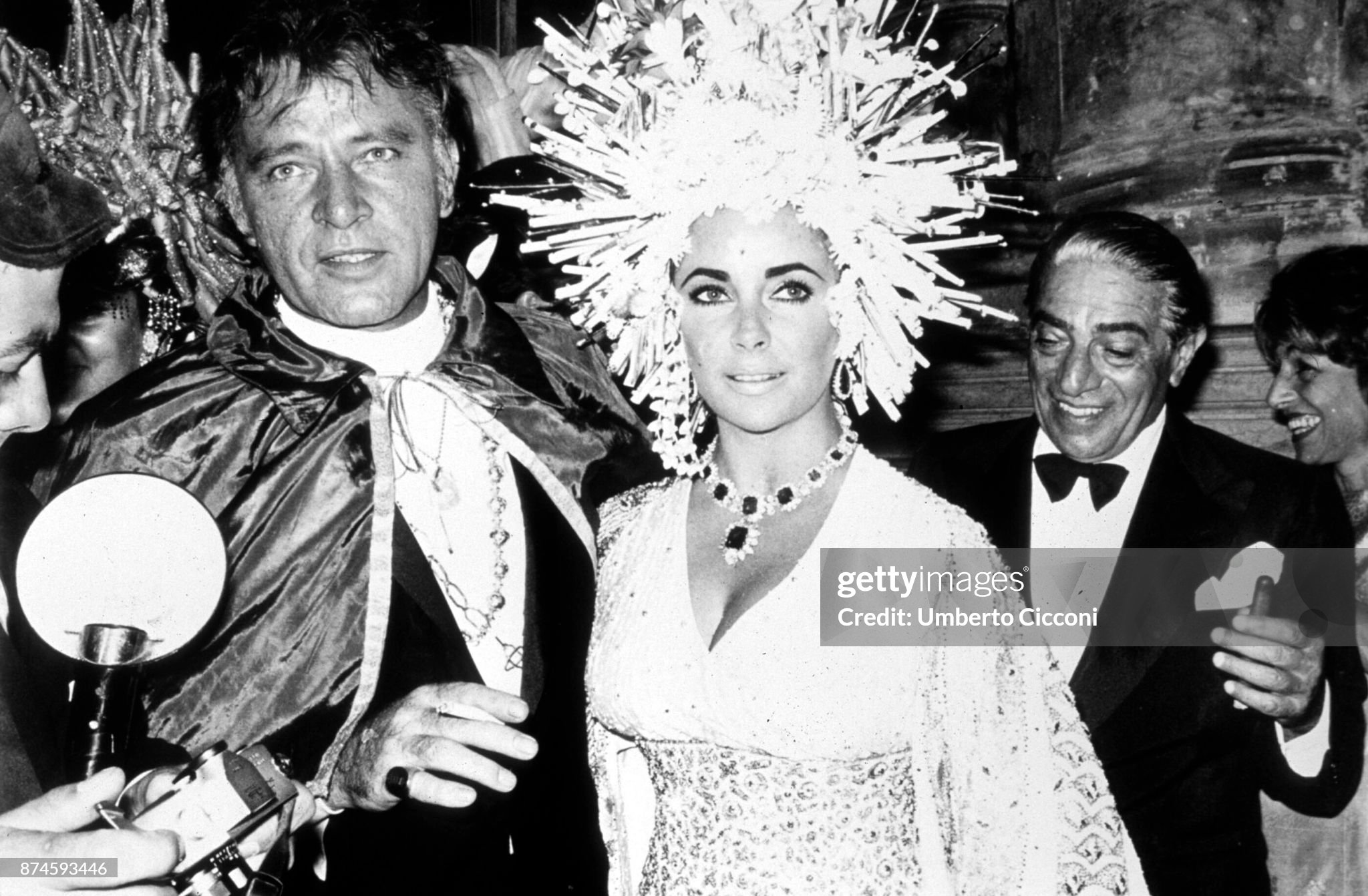 British-American actress Elizabeth Taylor (1932 - 2011), British actor Richard Burton (1925 - 1984) at 'Palazzo Rezzonico' for a masquerade party in Venice, Italy, in 1967. Behind them, Aristotle Onassis. 