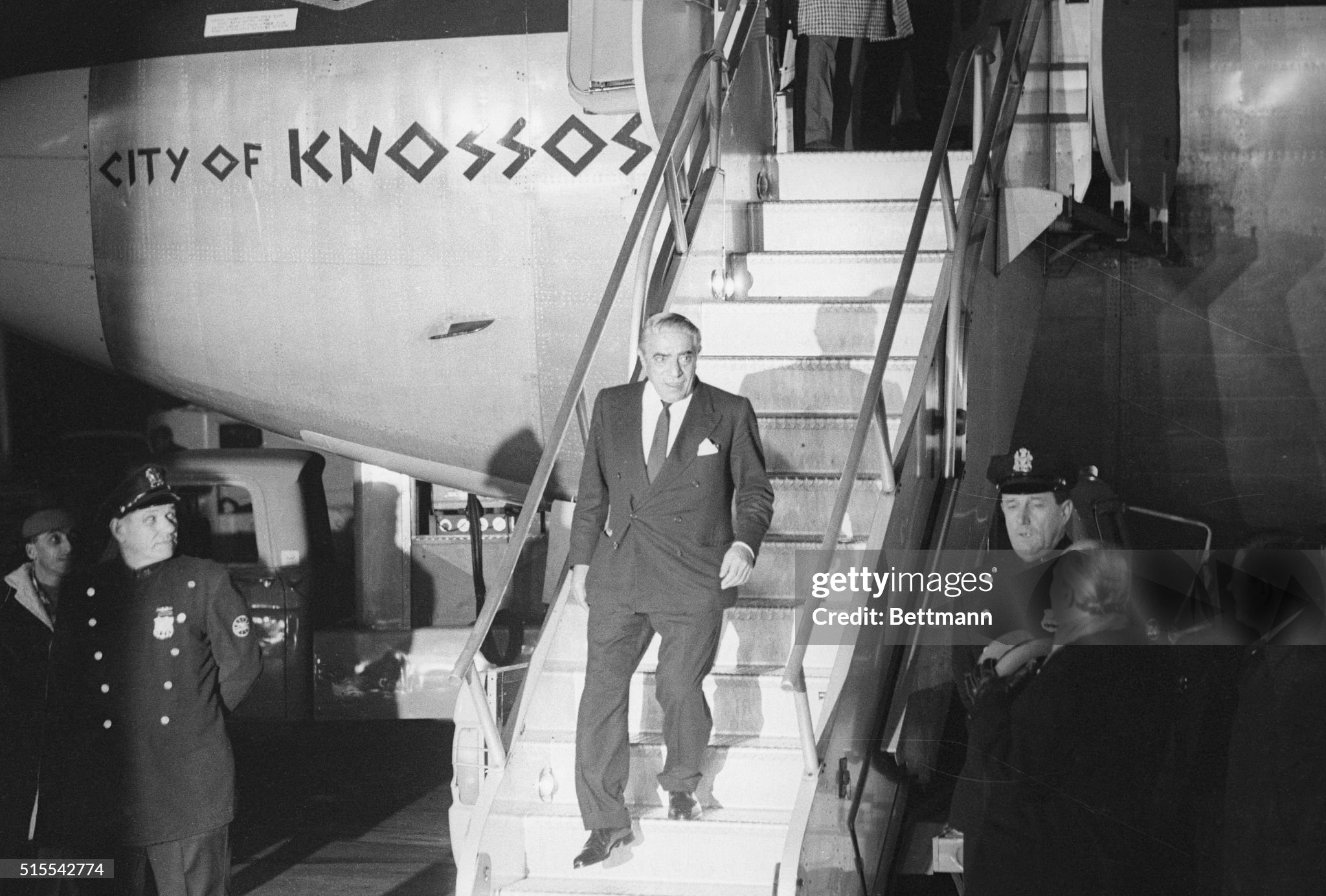 A New York City policeman looks on as Aristotle Onassis debarks from an Olympic Airways jetliner on arrival for a reunion with his bride of a month, the former Jacqueline Kennedy, on 22 November 1968. 