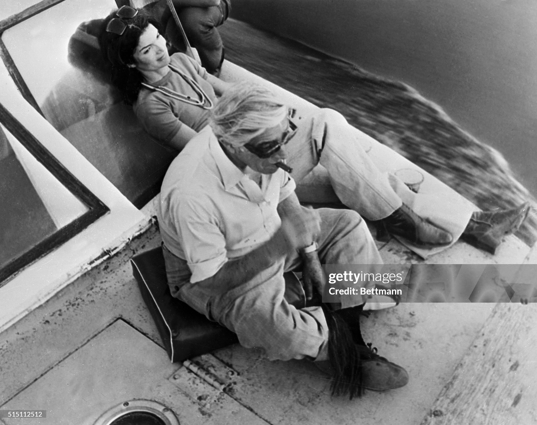 On a river trip down the Nile, Jacqueline Onassis relaxes and stretches out, while her husband, Aristotle, sits on a cushion and enjoys a cigar on 28 March 1974. 
