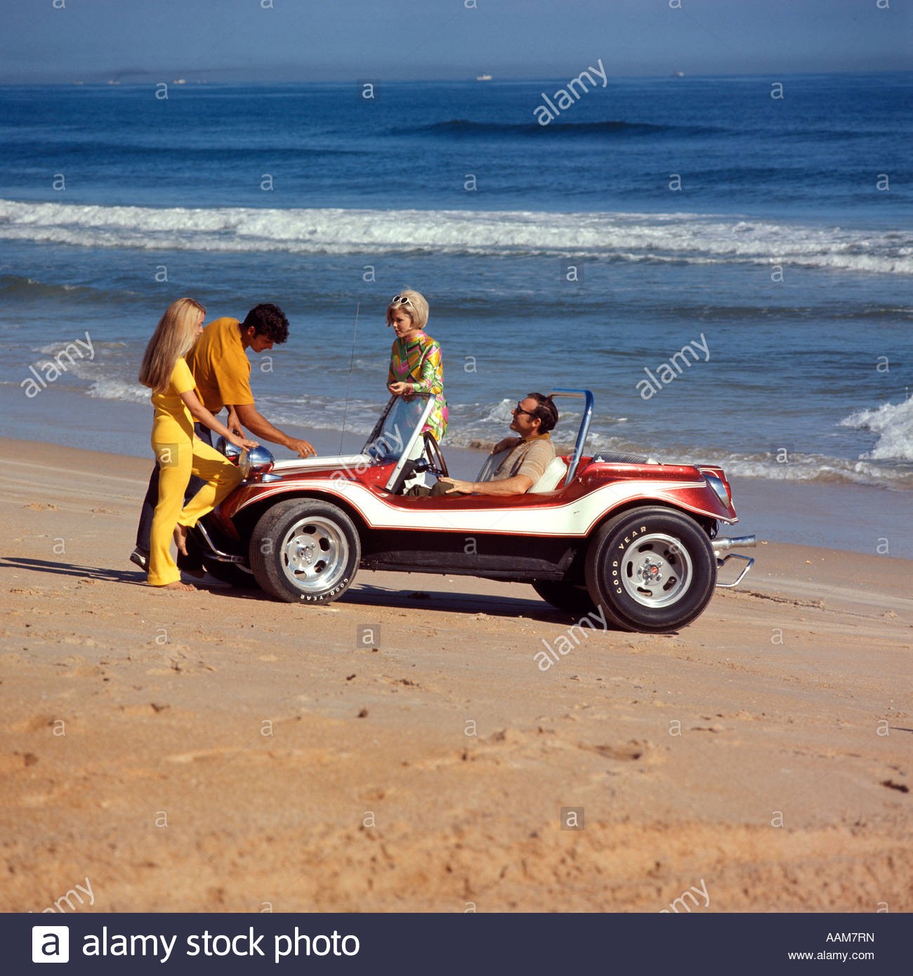 2 1970s couples on beach with a red white dune buggy.