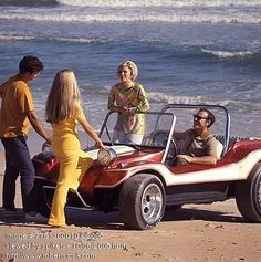 2 1970s couples on beach with a red white dune buggy.