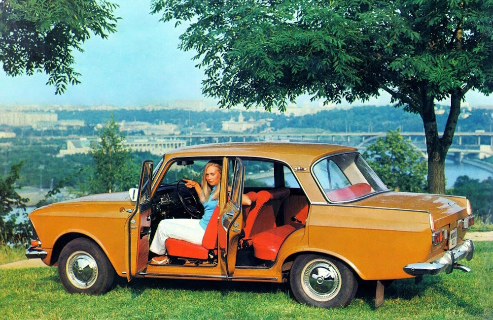 A blonde girl in an orange Moskvitch.