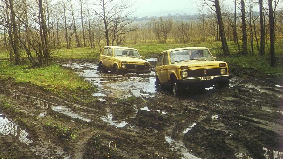 Two yellow Lada Nivas in the mud.