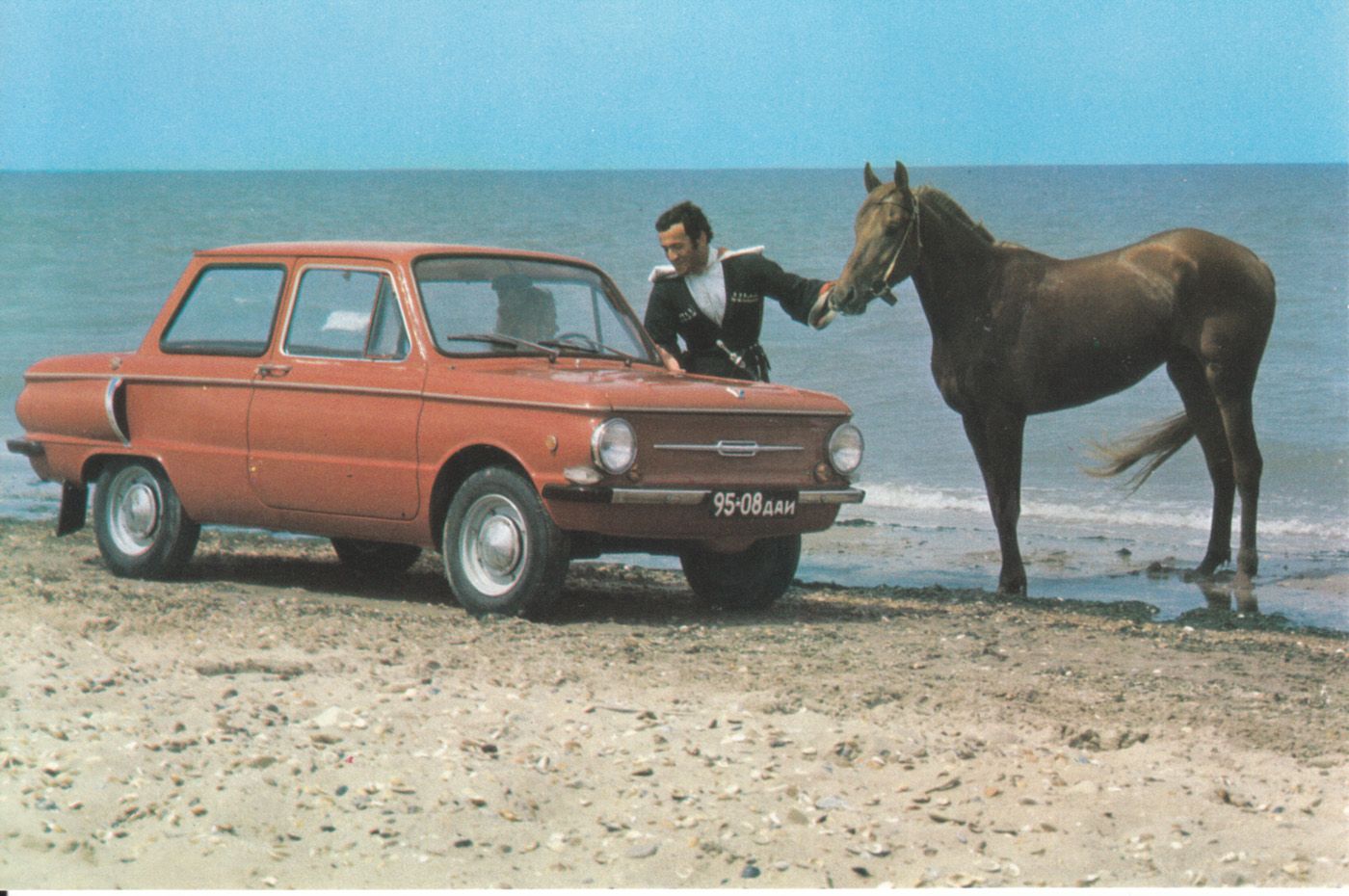 A woman in a red ZAZ-968A (1974-1979) talking to a man with a horse on a beach.