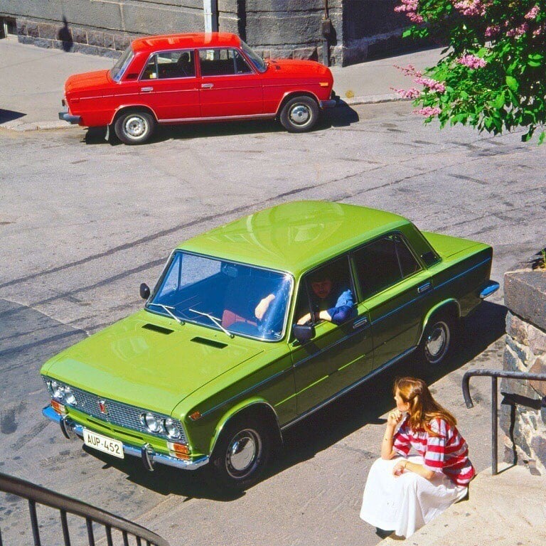 A girl and a man with a green and a red Lada.