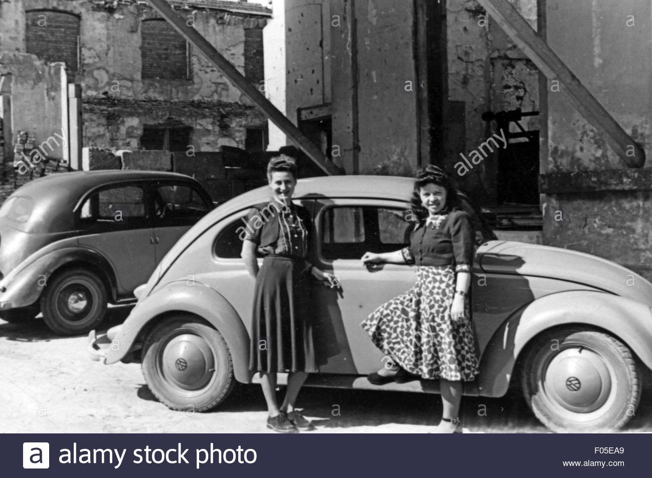 Leisure time excursion. Two women in front of VW Beetle having a break on a roadtrip in 1950s.