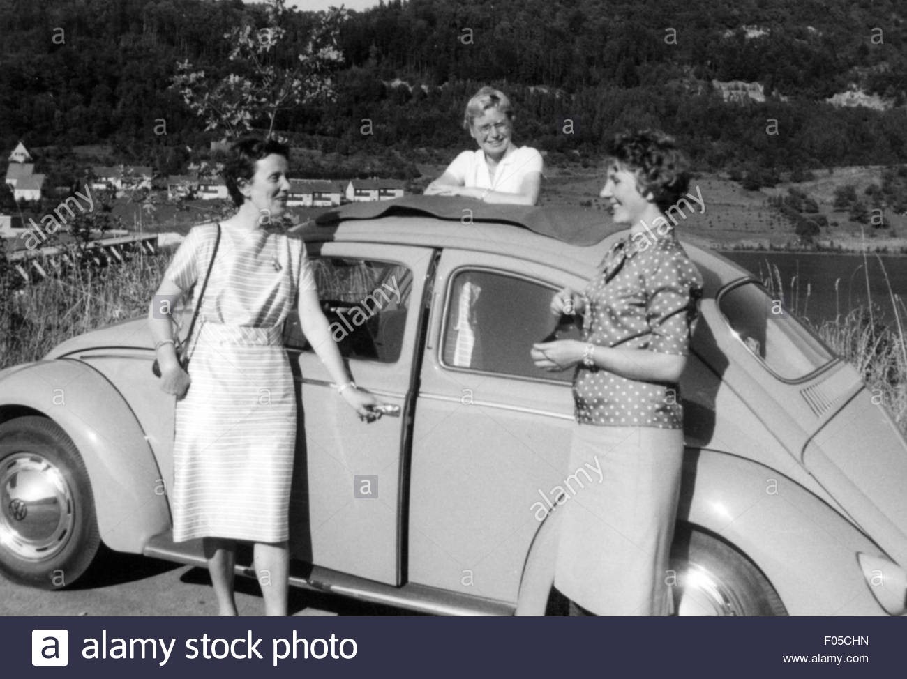 Leisure time excursion. Three women in front of VW Beetle having a break on a roadtrip in 1950s. 