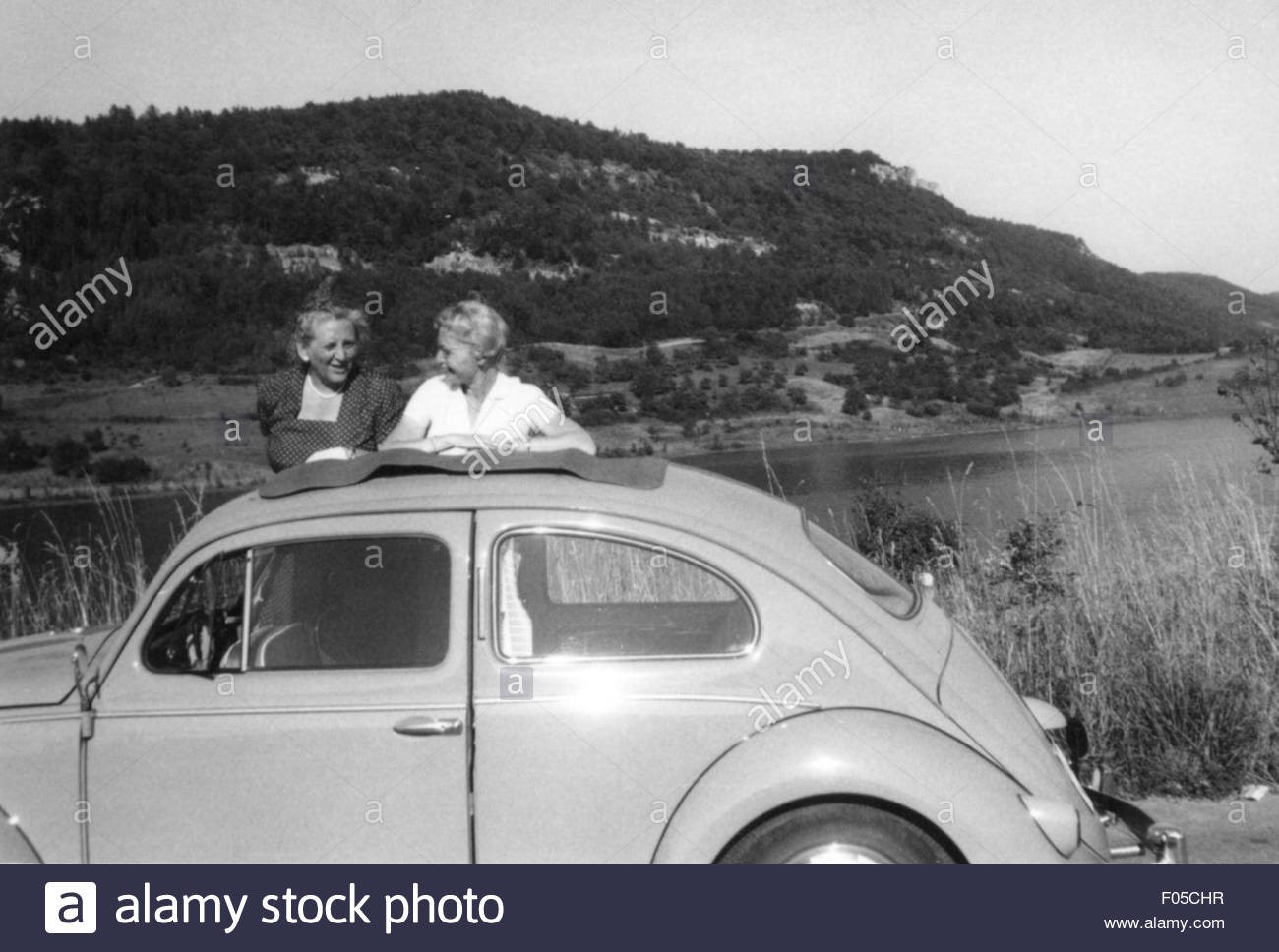 Leisure time excursion. Two women in front of VW Beetle having a break on a roadtrip in 1950s. 