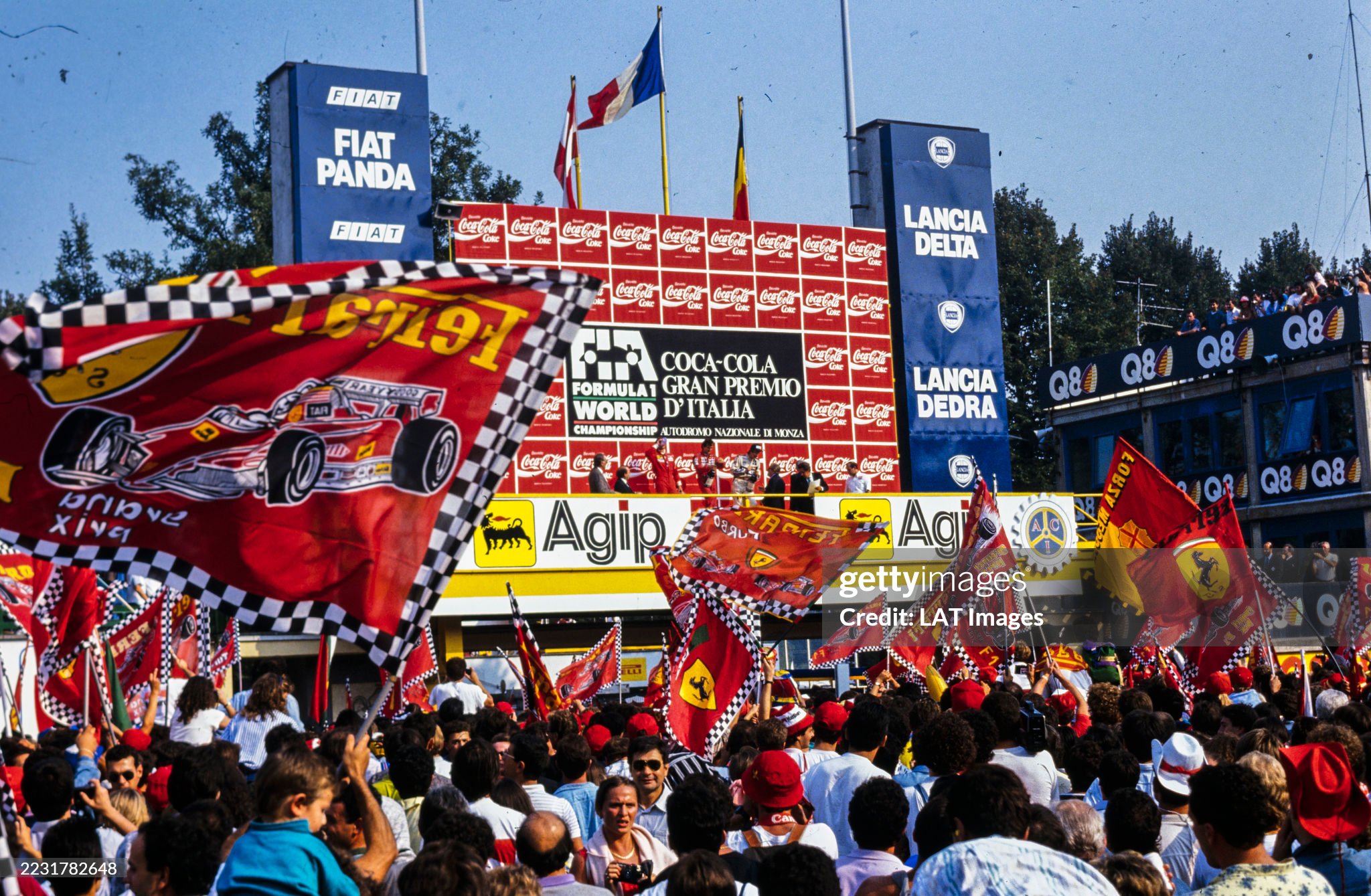Alain Prost, 1st position, Gerhard Berger, 2nd position, Thierry Boutsen, 3rd position and Jean-Marie Balestre, in conversation with Boutsen, on the podium in front of the tifosi and their flags after the Italian Grand Prix at Autodromo Nazionale Monza on 10 September 1989. 