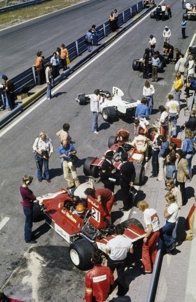 A view down the pit lane with James Hunt, Hesketh 308 Ford, heading out on track and Tom Belso, Williams FW02 Ford in the foreground.