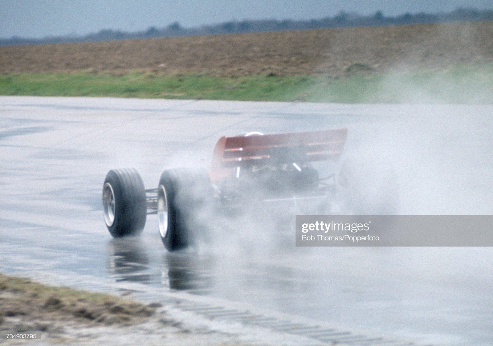 View of the Lotus 72 F1 racing car being driven in testing on the rain soaked track at Silverstone motor racing circuit near Towcester, England circa 1970. Racing drivers Jochen Rindt and John Miles would compete in the Lotus 72 car during the 1970 season.