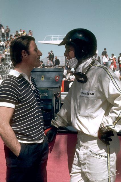 A casual Graham Hill, in conversation with a suited and helmeted Dan Gurney. 
