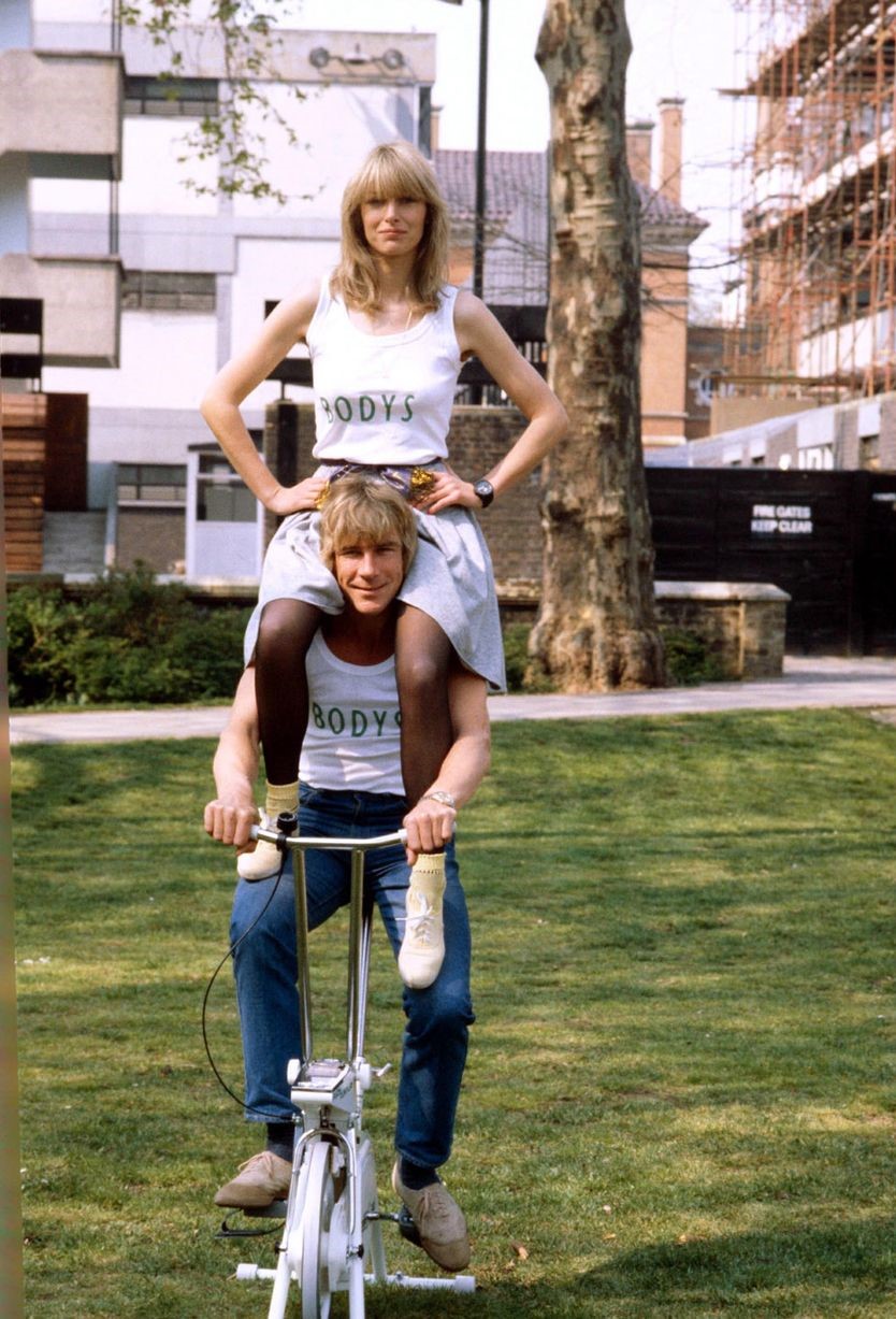 James Hunt poses on an exercise bicycle with ex-girlfriend Jane Birbeck on his shoulders to publicize the opening of their health club 'Bodys' on 10th May 1982.