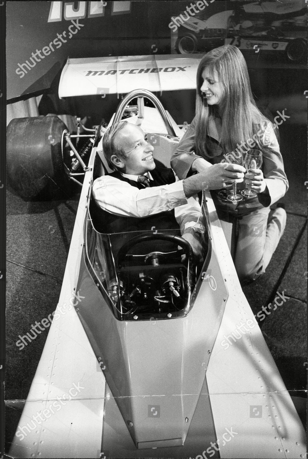 John Surtees in his new Formula 2 car gets a champagne toast from model Rebecca Shott.