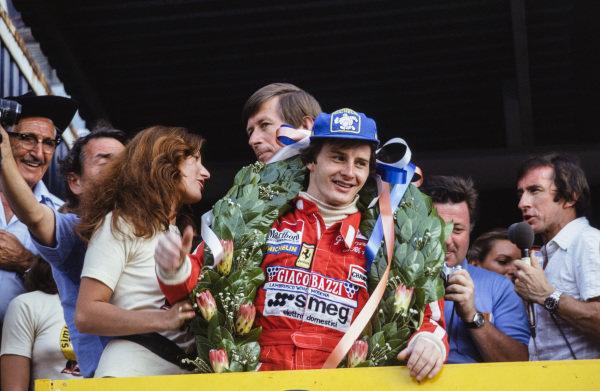 South African GP 1979 at Kyalami. Gilles Villeneuve celebrates victory on the podium as Jackie Stewart broadcasts on the right.