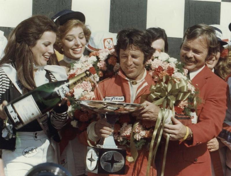 Mario Andretti on the podium with girls and champagne.