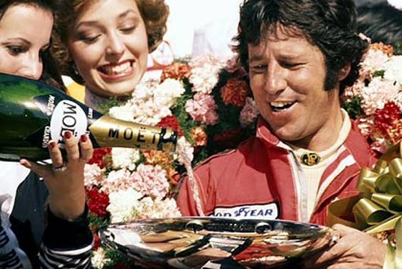 Mario Andretti on the podium with girls and champagne.