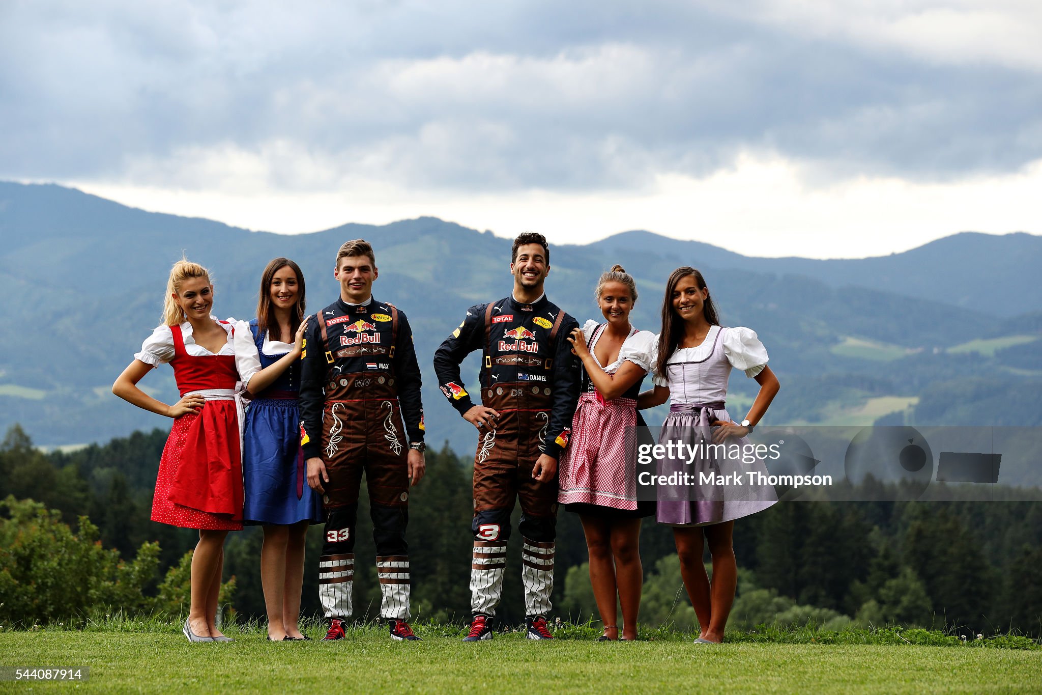 Daniel Ricciardo of Australia and Red Bull Racing and Max Verstappen of the Netherlands and Red Bull Racing pose with some girls in their lederhosen themed race suits during previews ahead of the Formula One Grand Prix of Austria at Red Bull Ring on 30 June 2016 in Spielberg, Austria. 