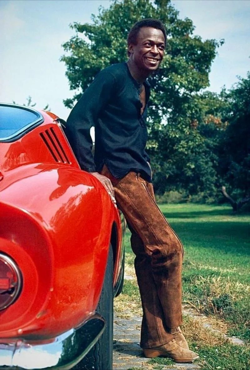 Miles Davis leans on his red Ferrari 275 GTB.