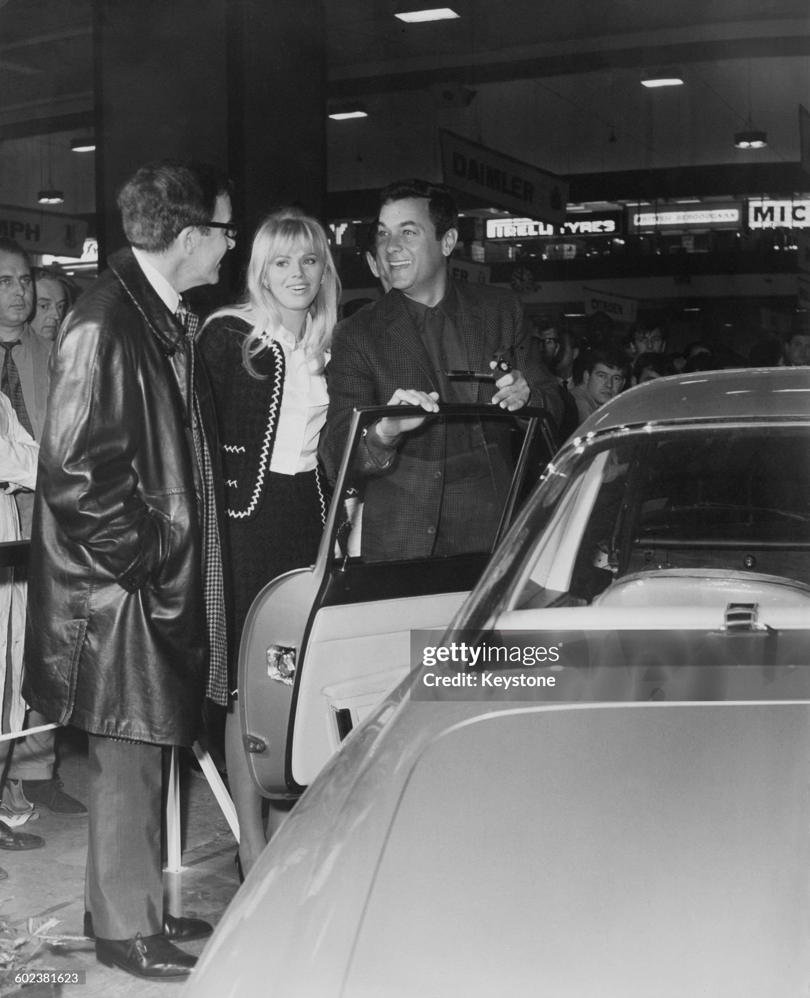 Left to right: British comic actor Peter Sellers, his wife, Swedish actress Britt Ekland and American actor Tony Curtis with a Ferrari 500 Superfast coupe, which Sellers has just bought for eleven and a half thousand pounds, at a preview of the Motor Show, Earls Court, London, 19th October 1965.