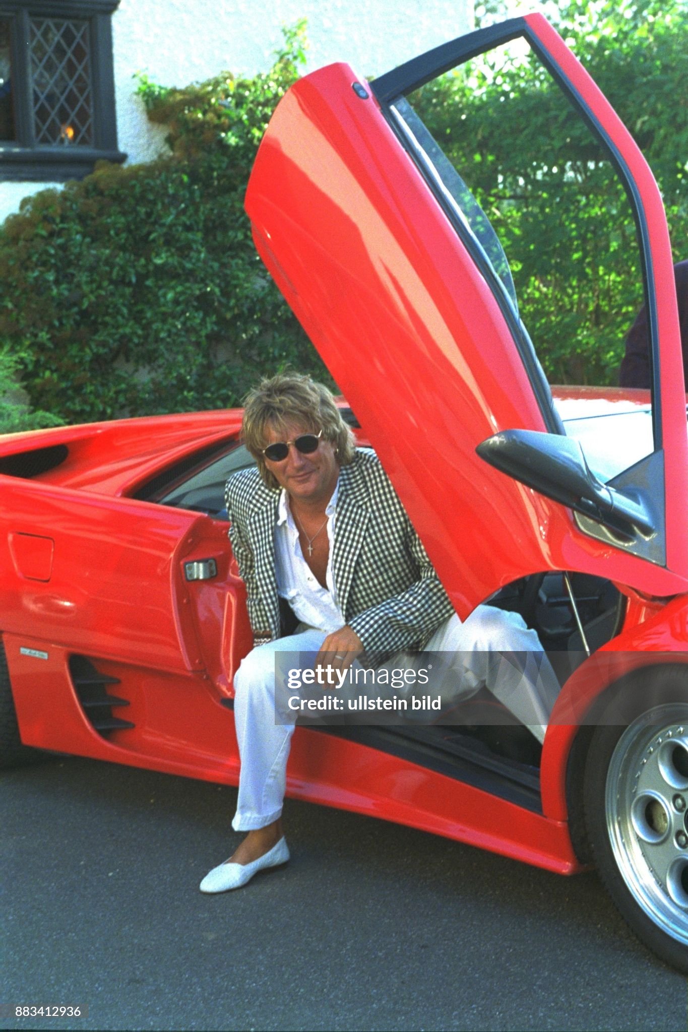 Rock singer Rod Stewart gets out of his car, a red Ferrari. 