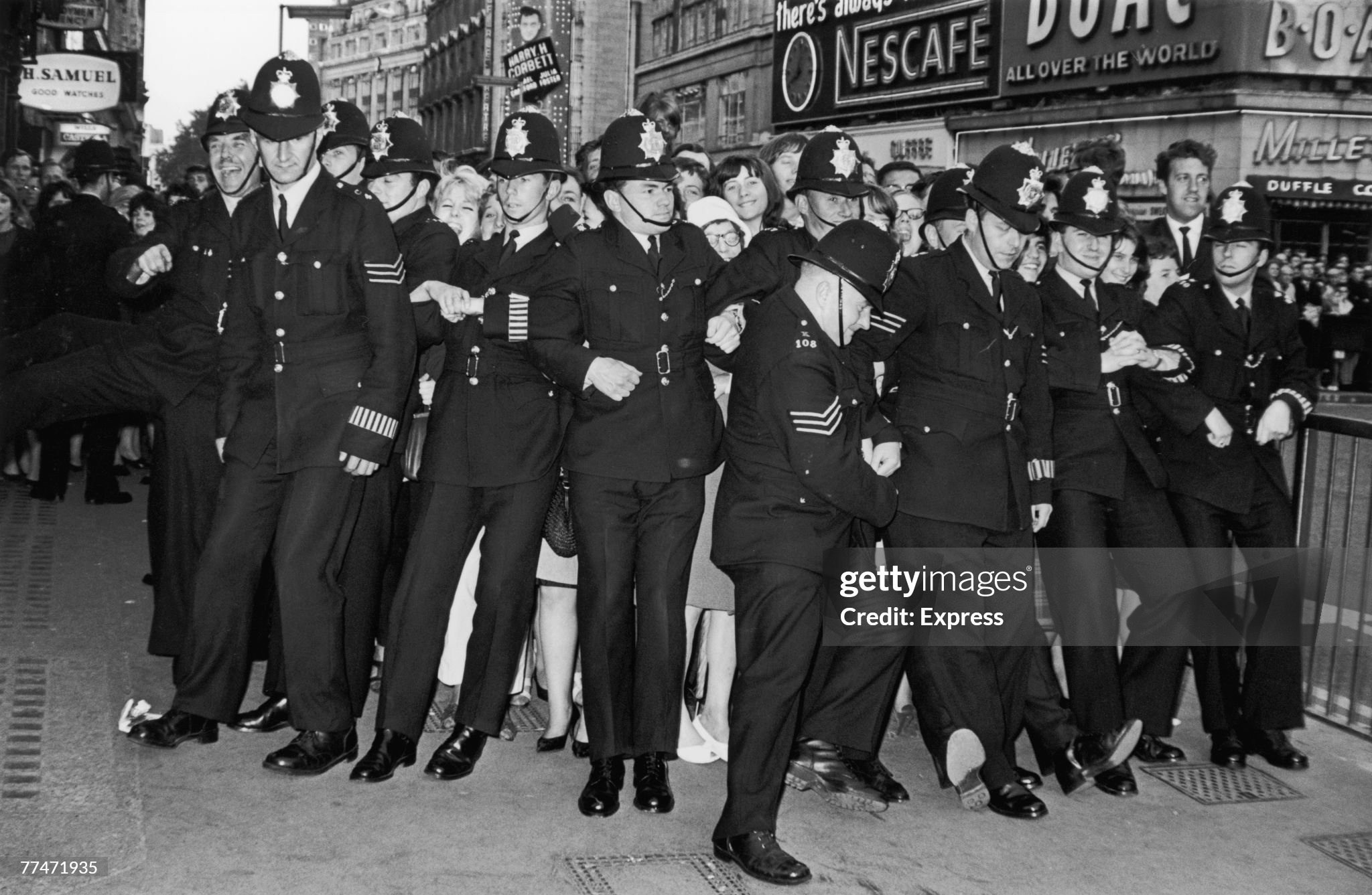 Policemen form a line to restrain female fans during the premiere of the new Beatles film 'Help!' at the London Pavilion, Piccadilly Circus, 29th July 1965. 