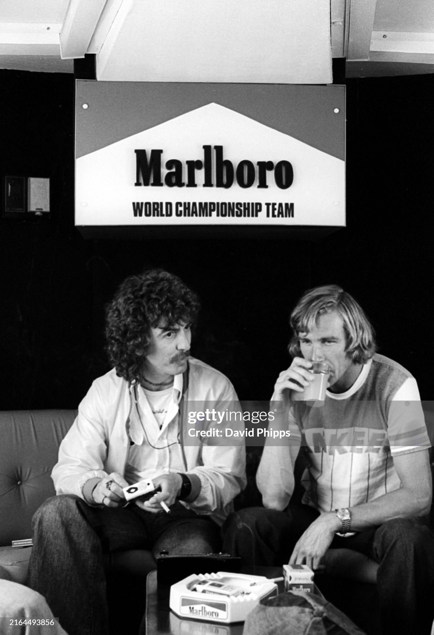 George Harrison enjoys a cigarette and a chat with race retiree James Hunt, McLaren, in the Marlboro motorhome at the Spanish Grand Prix in Jarama on 08 May 1977. 