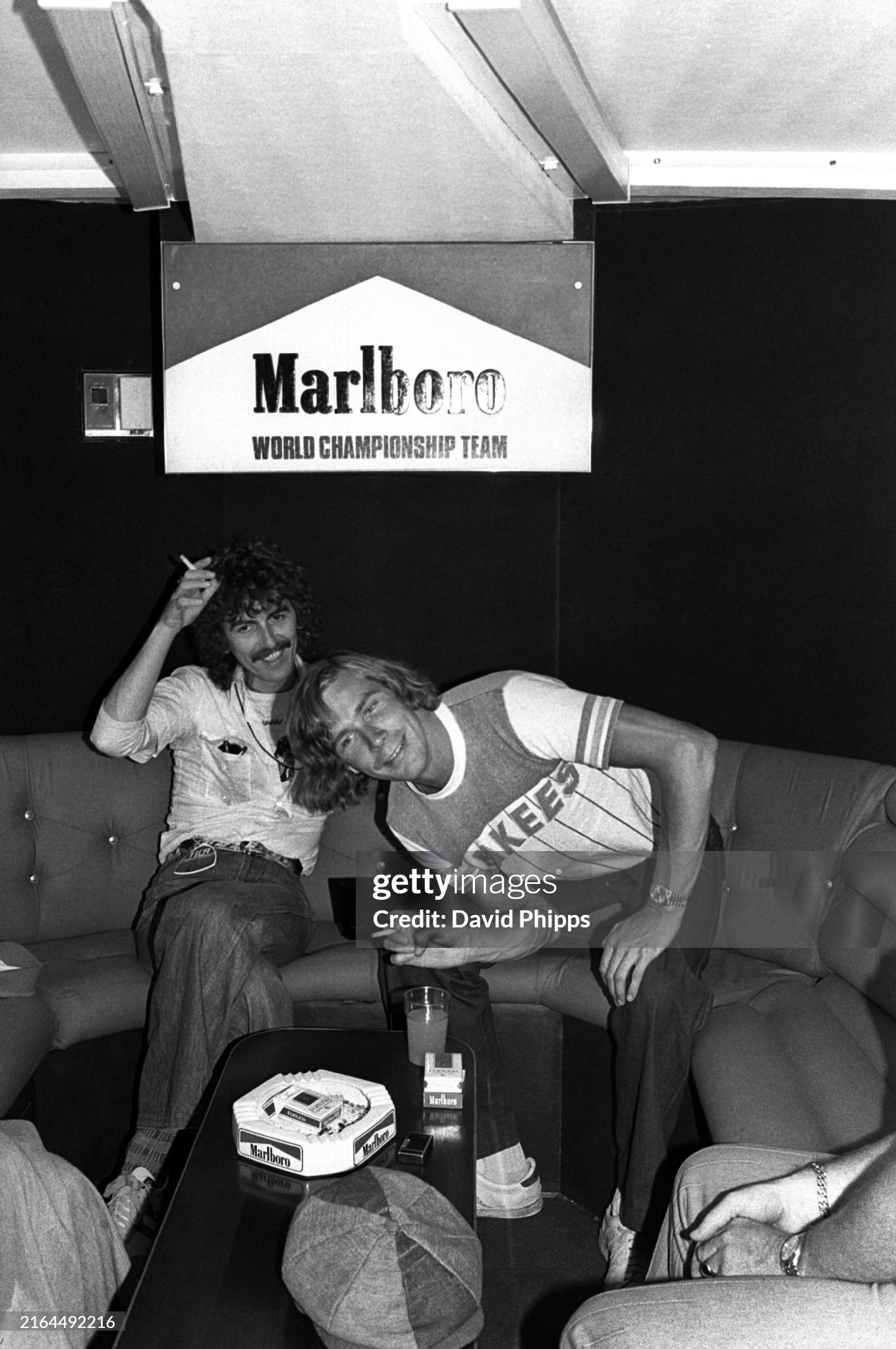George Harrison enjoys a cigarette and a chat with race retiree James Hunt, McLaren, in the Marlboro motorhome at the Spanish Grand Prix in Jarama on 08 May 1977. 