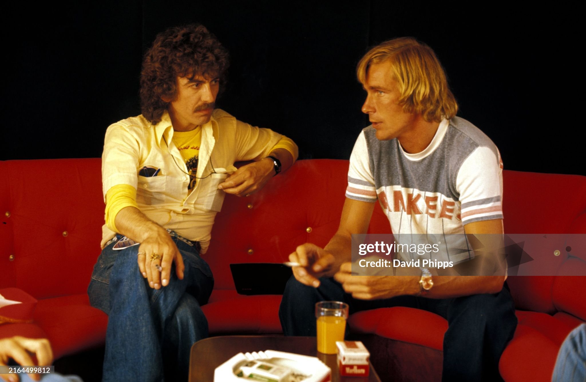 George Harrison enjoys a cigarette and a chat with race retiree James Hunt, McLaren, in the Marlboro motorhome at the Spanish Grand Prix in Jarama on 08 May 1977. 