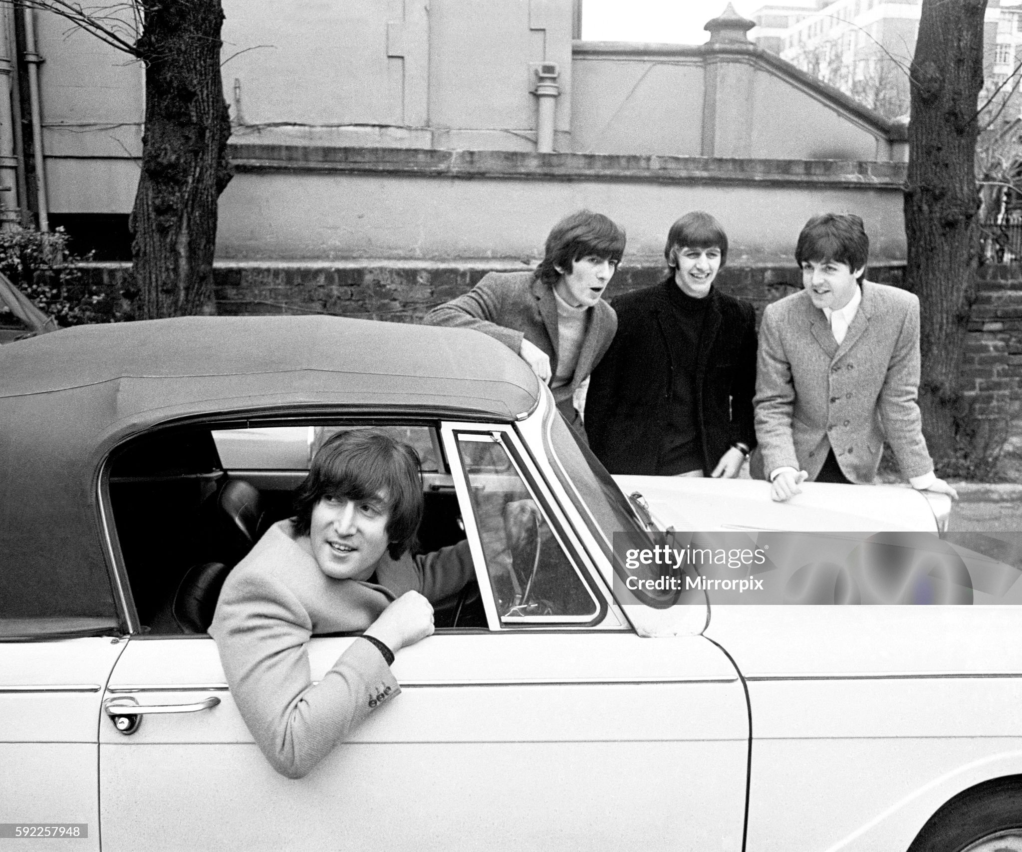 John Lennon passes his driving test in Weybridge on 15 February 1965. Paul McCartney, Ringo Starr and George Harrison are there to congratulate him. 