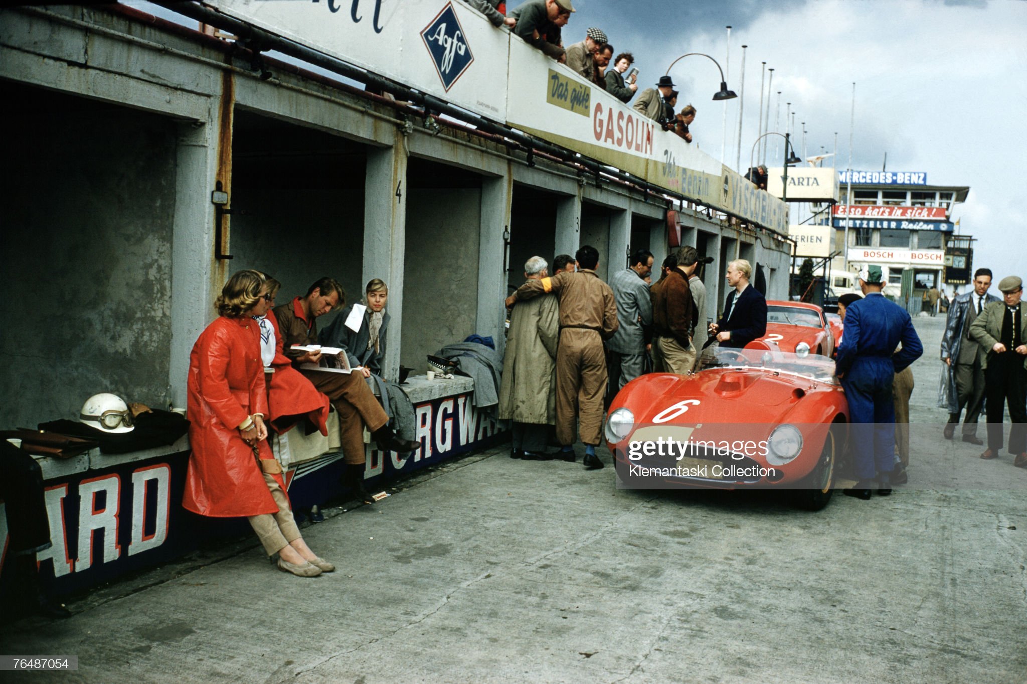 Mike Hawthorn standing next to his car in conversation with team manager Romolo Tavoni and others in the Ferrari pits during practice at the Nurburgring 1000 km Race, Nurburgring, 26th May 1957. 