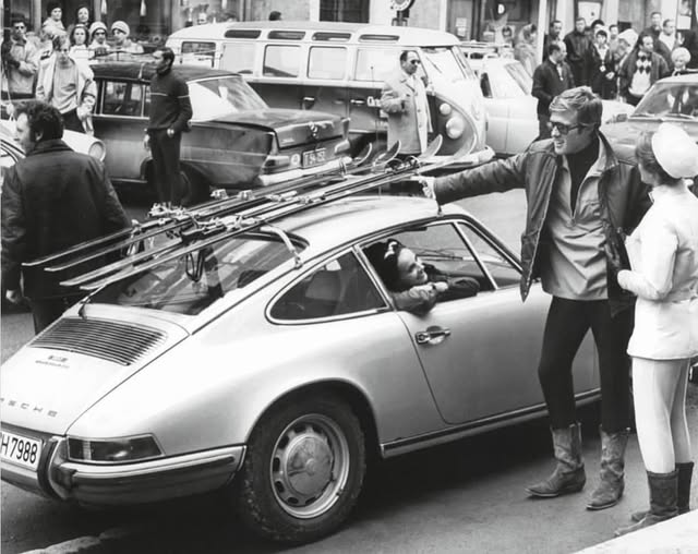 Robert Redford in front of a Porsche with skis on the roof.