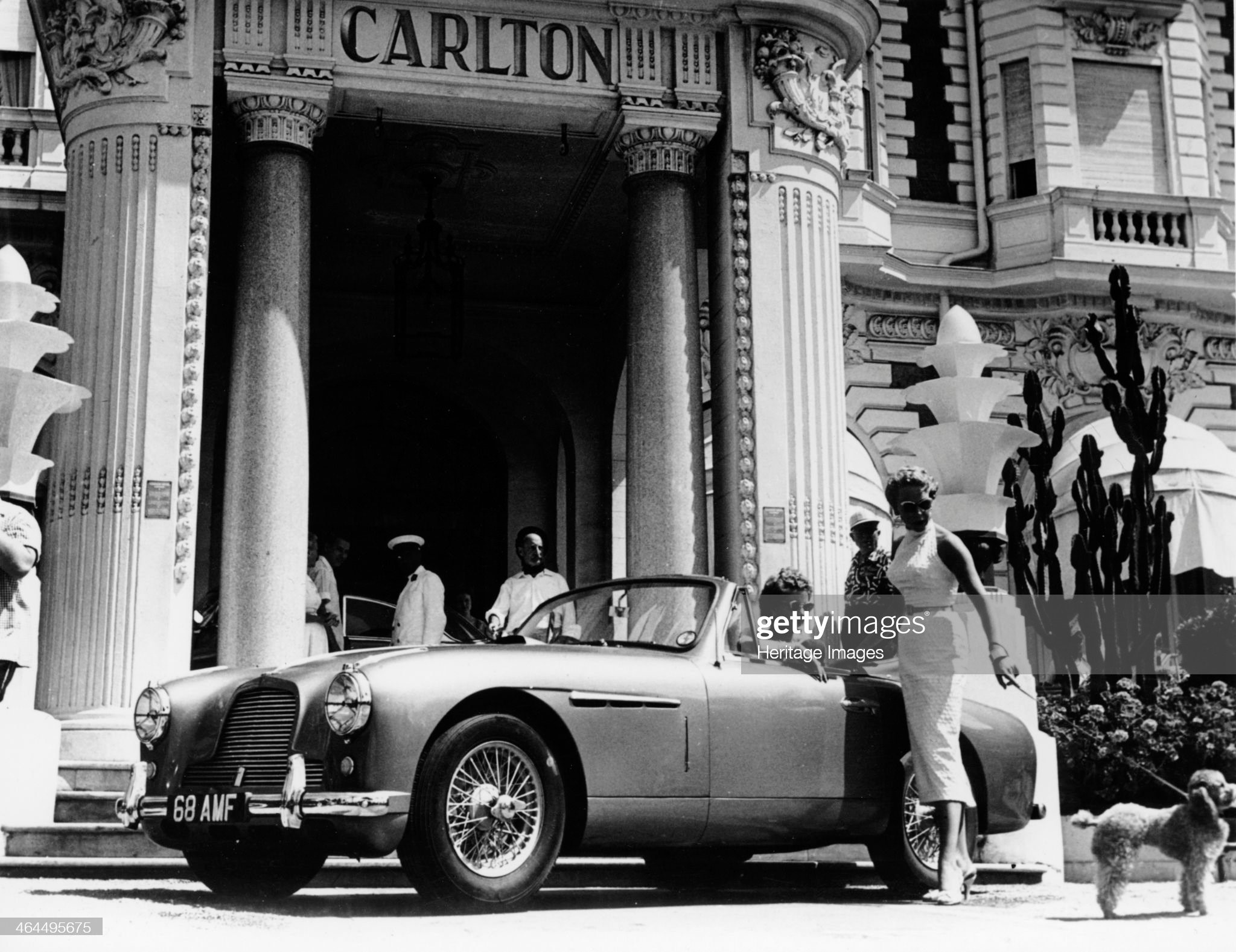 Aston Martin DB2-4 outside the Hotel Carlton, Cannes, France, 1955. A glamorous woman stands by the car with her poodle. This model was first shown at the London Motor Show in 1953 and was produced from 1953-1955. 